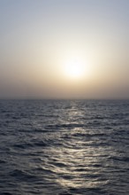 Background image, setting sun with silhouette of land, water surface in evening light, waves in the