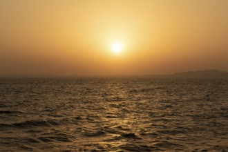 Background image, setting sun with silhouette of land, water surface in evening light, waves in the