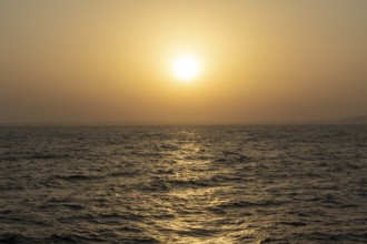 Background image, setting sun with silhouette of land, water surface in evening light, waves in the