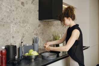 A young woman roasting duck breast in a sleek kitchen. The sunlight illuminates the modern space as