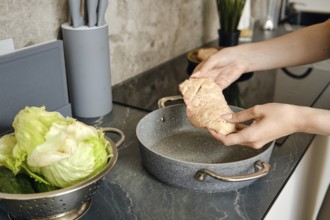 Hands gently hold a piece of duck above a cooking pot in a contemporary kitchen. Nearby, a bowl of