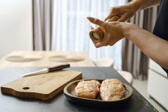 A person seasons fresh duck fillets with sea salt in a stylish kitchen. The wooden cutting board