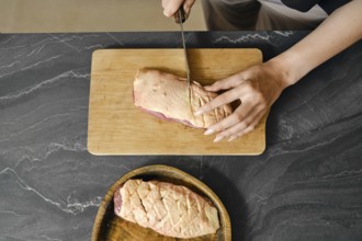 Overhead view of a hand skillfully cuts crosswise raw duck meat on a wooden cutting board