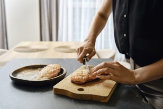 A person skillfully slices fresh duck fillets on a wooden cutting board in a modern kitchen