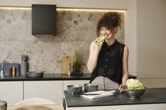 Smiling woman enjoying a fresh salad in a modern kitchen while preparing healthy meals