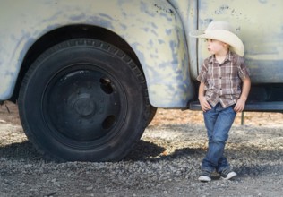Young boy wearing cowboy hat relaxing leaning against antique truck