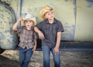Two young boys wearing cowboy hats leaning against antique truck