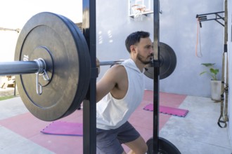 Focused male athlete lifting weights and performing squats in a home gym, showcasing strength and