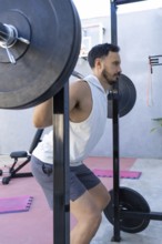 Focused male athlete is strengthening his legs by performing squats with a weighted barbell in a