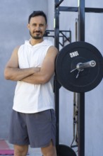 Sporting a confident expression, a sportsman with crossed arms leans against a weight plate in an