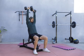 Focused athlete lifting dumbbells while seated on a bench in an outdoor gym, demonstrating strength