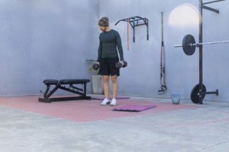 Young sportsman lifting two black dumbbells while engaging in a workout in a private outdoor gym,