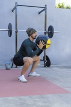 Young sportsman performing squats with a medicine ball in an outdoor gym, demonstrating strength