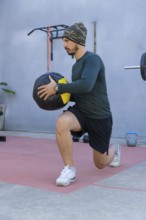 Athlete wearing a beanie, long-sleeved shirt, and shorts performs lunges while holding a medicine