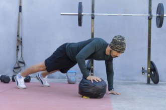 Focused athlete is doing push-ups with one hand on a medicine ball in an outdoor gym, showcasing