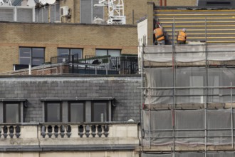 Two workmen in high viz orange jackets on scaffolding on a building, City of London, England,