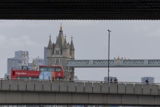 Red double decker bus driving over a bridge with Tower bridge in the background, City of London,