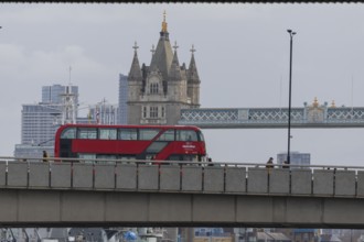 Red double decker bus driving over a bridge with Tower bridge in the background, City of London,