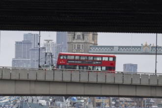 Red double decker bus driving over a bridge with Tower bridge in the background, City of London,