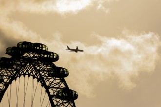 The London Eye wheel with a jet aircraft flying behind at sunset, City of London, England, United