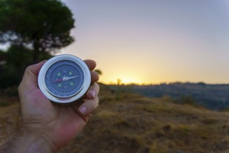 Hand is holding a compass showing direction at sunset in the nature