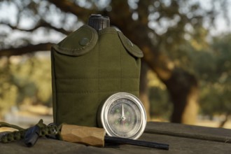 Survival gear including canteen, compass, fire starter and whistle are laying on a wooden table