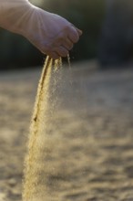 Hand pouring sand at sunset, symbolizing the passage of time and the ephemeral nature of life
