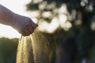 Hand pouring sand with sunset bokeh in the background, representing the passage of time
