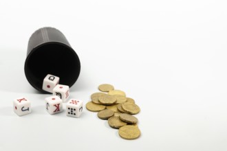 Poker dice and coins spilling from a dice cup on a white background represent gambling and