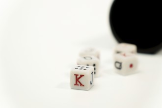 Poker dice showing king, jack, queen and ten on white background with black cup