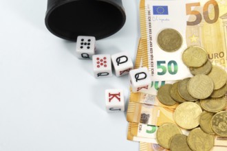 Poker dice spilling from a black cup onto a pile of fifty euro banknotes and coins, symbolizing