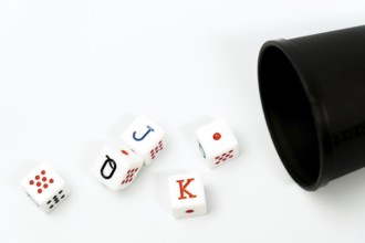 Poker dice spilling from a black dice cup onto a white background, representing gambling and games