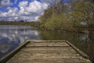 Wooden footbridge at the lake (Krickenbecker Seen) with trees and cloudy sky in spring, Nettetal