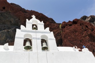 Agios Nikolaos Mavrorachidi, chapel with bell tower in front of red rock face, volcanic rock,