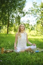 A woman peacefully meditates on a mat in a vibrant green park, surrounded by trees and nature