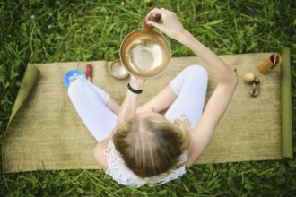 Overhead view of a woman sitting cross-legged on a mat, skillfully playing a singing bowl.