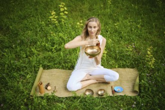 A person sits cross-legged on a mat surrounded by singing bowls, engaging in a meditation practice.
