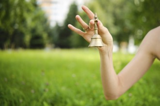 A hand gracefully holds a singing bell in a vibrant green garden, with soft sunlight filtering