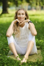 A woman sits peacefully on a mat in a lush park, enjoying a moment of tranquility. She is dressed