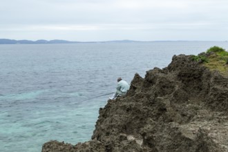 Angler at Sesoko's tail, rock formation, rugged cliffs of volcanic rock at the southern tip of