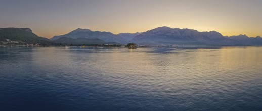 Panoramic dusk scene in Kemer, Turkey, showing the town illuminated coastline and beach, reflected