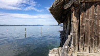 Wooden hut directly on the lake with blue sky and scattered clouds, pile dwellings Unteruhldingen
