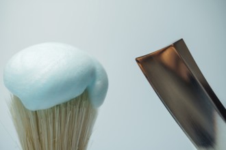 Shaving brush with light blue foam and metal razor blade ready for skincare routine