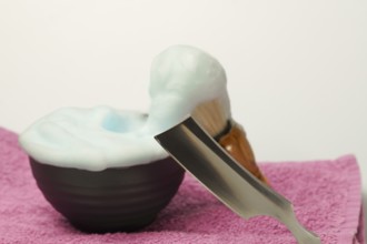 Shaving foam overflowing from a bowl with a straight razor and shaving brush resting on a pink