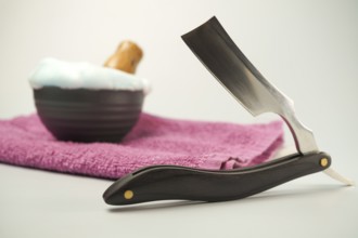 Shaving accessories including a straight razor, shaving soap, and pink towel evoke a sense of