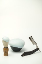 Shaving foam in a bowl, shaving brush and a straight razor are arranged on a white background,