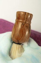 Wooden shaving brush dipped in light blue foam on a purple towel, evoking a sense of luxury and