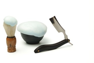 Shaving foam, brush, and straight razor are creating a grooming still life on a white background