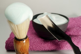 Shaving brush, razor and shaving cream resting on pink towel