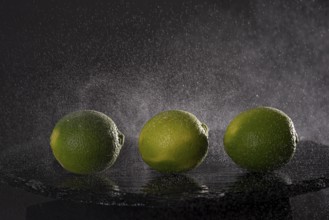 Three limes on a stone slab with drops of water